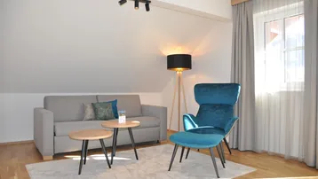 Helles Wohnzimmer mit gemütlichem Sofa, modernem Sessel und Holzboden unter einer Dachschräge.