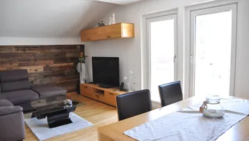 Helles Wohn- und Esszimmer mit Holzboden, moderner Einrichtung und Zugang zum Balkon.
