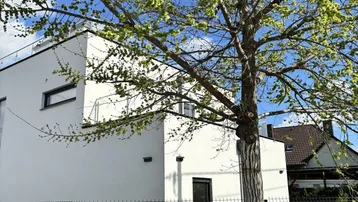 Modernes weißes Gebäude mit Flachdach, großen Fenstern und Klimaanlage im Außenbereich.