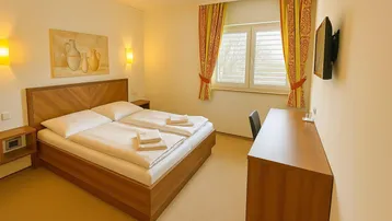 Helles Schlafzimmer mit zwei Einzelbetten, Holzmöbeln und einem Fenster mit Jalousien.
