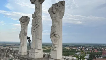 Alte Steinskulpturen auf einer Mauer mit weitem Panoramablick über die ländliche Landschaft und ein Dorf.