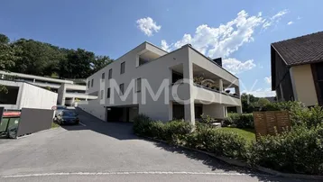 Moderne Wohnanlage mit mehreren Etagen, Balkonen und Zufahrt zur Tiefgarage, umgeben von viel Grün.