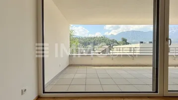 Heller Innenraum mit Holzboden und großem Fenster, das auf eine Terrasse mit Bergblick führt.