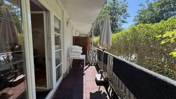 Langer, schmaler Balkon mit dunklen Fliesen, Sonnenschirm und Blick ins Grüne.
