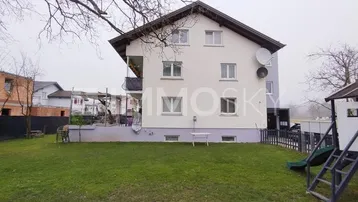 Mehrfamilienhaus mit Garten, Rasenfläche und kleinem Spielplatz im Außenbereich.