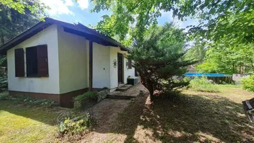 Kleines Haus im Grünen mit sichtbarem Pool im Hintergrund, umgeben von Bäumen und Natur.
