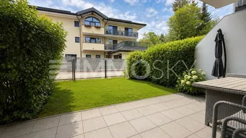Gepflasterte Terrasse mit Gartenmöbeln und Blick auf die gepflegte Grünfläche und das Gebäude.
