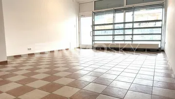 Geräumiger, heller Ladenbereich mit kariertem Fliesenboden und großen Schaufenstern zur Straße.