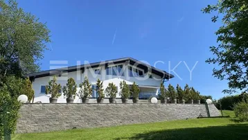 Modernes Haus mit weißer Fassade, großen Fenstern und gepflegtem Gartenbereich unter blauem Himmel.