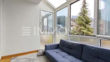 Heller Wintergarten mit blauer Couch, großen Glasfenstern und Bergblick.