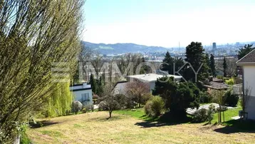 Weitläufiges Grundstück mit grüner Wiese und Fernblick auf die Stadt und Berge.