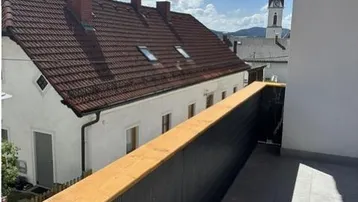 Blick von einem Balkon auf die Dächer der Stadt und einen Kirchturm unter blauem Himmel.