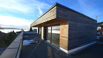 Moderne Architektur mit Holzfassade und großer Dachterrasse unter blauem Himmel.