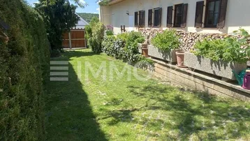 Außenansicht des Hauses mit gepflegtem Rasen, Hecke und gestapeltem Brennholz unter den Fenstern.
