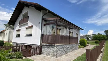 Außenansicht des Hauses mit überdachter Terrasse, Steinfassade und gepflegtem Vorgarten.