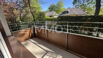 Heller Balkon mit Metallgeländer und Blick ins Grüne sowie auf umliegende Häuser.