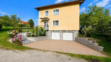 Gelbes Einfamilienhaus mit Doppelgarage, gepflasterter Auffahrt und Außentreppe.