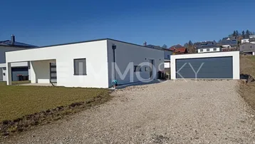 Moderne weiße Villa mit Flachdach, Kiesauffahrt und separater Garage unter blauem Himmel.