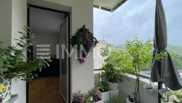Ein gemütlicher Balkon mit vielen Pflanzen, einem Sonnenschirm und Blick ins Grüne.