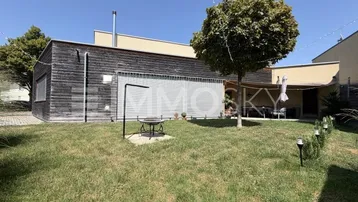 Moderner Gartenbereich mit Rasenfläche, Feuerstelle und überdachtem Sitzbereich am Haus.
