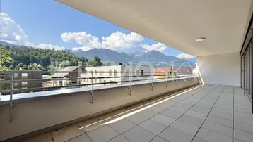 Große, geflieste Terrasse mit Metallgeländer und beeindruckendem Bergblick unter blauem Himmel.