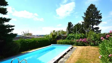 Großer Außenpool im Gartenbereich mit umliegender Grünfläche und sonnigem Himmel.