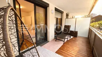 Sonniger Balkon mit Holzfußboden, Hängesessel und Blick in den Innenbereich.