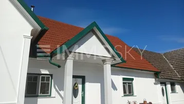 Eingangsbereich eines frisch renovierten Hauses mit weißer Fassade, rotem Ziegeldach und grünen Akzenten.