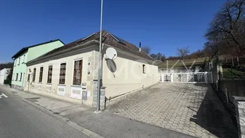 Altes Gebäude mit heller Fassade und gepflasterter Einfahrt unter blauem Himmel.