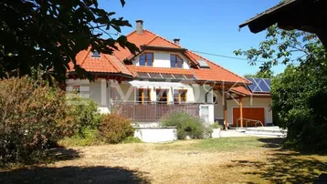 Einfamilienhaus mit rotem Ziegeldach, Balkon und Photovoltaikanlage auf dem Nebengebäude.
