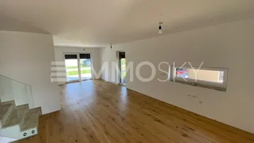 Helles, leeres Wohnzimmer mit Holzboden, großen Fenstern und Zugang zur Terrasse.
