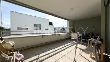 Geräumiger überdachter Balkon mit Fliesenboden, Sitzgelegenheiten und Blick auf die Umgebung.