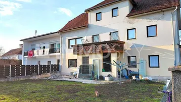 Mehrstöckiges Wohnhaus mit Gartenbereich und Balkonen unter blauem Himmel.