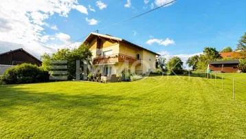 Freistehendes Haus mit großem grünen Garten und Balkon unter blauem Himmel.