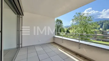 Geräumiger Balkon mit Fliesenboden, Blick ins Grüne und auf die Berge unter blauem Himmel.