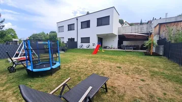Moderner Neubau mit großem Garten, Trampolin, Rutsche und überdachtem Sitzbereich im Freien.