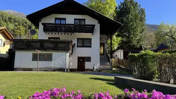 Traditionelles Einfamilienhaus mit weißer Fassade, Holzbalkonen und gepflegtem Vorgarten in ländlicher Umgebung.