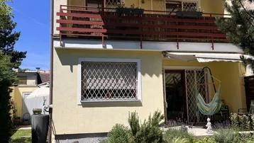 Gelbe Hausfassade mit Balkon im Obergeschoss und einer Terrasse im Erdgeschoss mit Schaukelstuhl.