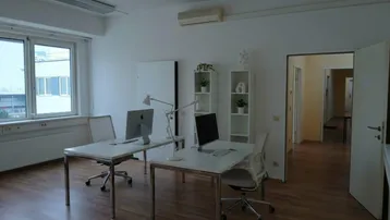 Modernes Büro mit zwei Arbeitsplätzen, Holzfußboden und Blick nach draußen durch große Fenster.