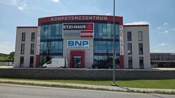 Modernes Geschäftshaus mit großer Glasfassade und "For Sale"-Schildern an der Vorderseite.