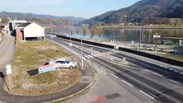 Luftaufnahme einer Straße entlang eines Flusses mit Bergen im Hintergrund und einem Maklerbanner.