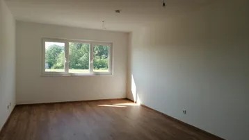 Helles, leeres Zimmer mit Holzboden und Blick ins Grüne, bereit zur individuellen Gestaltung.