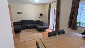 Geräumiger Wohn-Essbereich mit großem Ecksofa, Holzboden und Zugang zum Außenbereich.