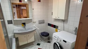 Badezimmer mit farbenfrohen Fliesen, Holzbalkendecke und integrierter Waschmaschine.
