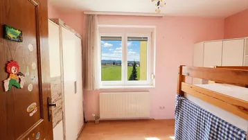 Helles Kinderzimmer mit Etagenbett, Schrank und weitem Blick ins Grüne.