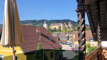 Gemütlicher Balkon mit Holzelementen, Sonnenschirm und weitem Blick auf das Dorf und ein Schloss.