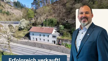 Historisches Einfamilienhaus an einem Hang mit Blick auf eine Brücke und grüne Landschaft.