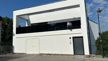 Moderne weiße Fassade eines Neubaus mit Balkon und Glasgeländer unter blauem Himmel.