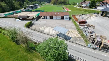Luftaufnahme des Anwesens mit Sportplätzen, einem Gebäude und umliegender grüner Landschaft unter blauem Himmel.