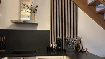 Moderne Küche mit dunkler Arbeitsplatte, integriertem Backofen und einer Holzlamellenwand neben der Treppe.